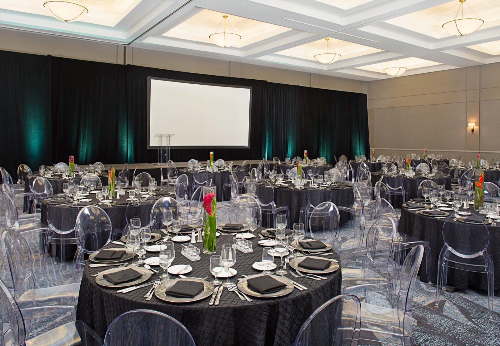 Gala dinner set with dark linens, ghost chairs, and stage screens